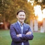 Confident businessman smiling outdoors at sunset, dressed in a formal suit.